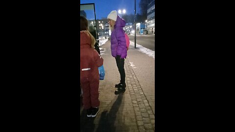 Beautiful young woman in a short down jacket freezes while waiting for the bus.