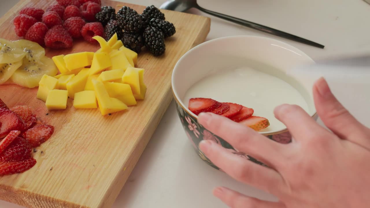 Preparing a bowl with yogurt and assorted freshly chopped fruit.