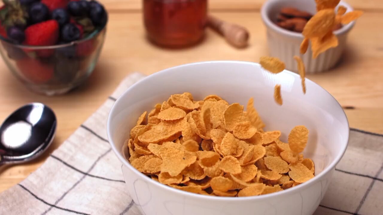 Delicious corn flakes fall in slow motion into a pristine white bowl on the table