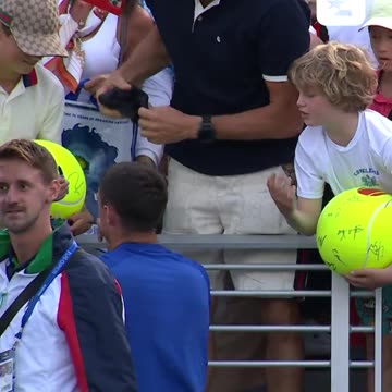 US Open, a professional tennis player tries to hand a hat to a young fan, but an adult takes it.
