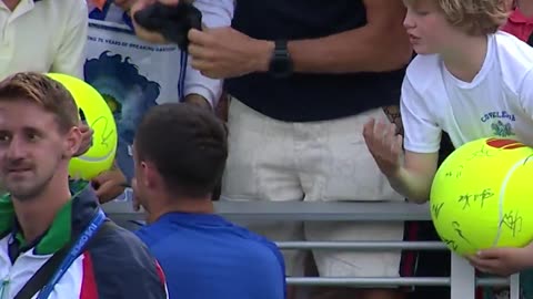 US Open, a professional tennis player tries to hand a hat to a young fan, but an adult takes it.