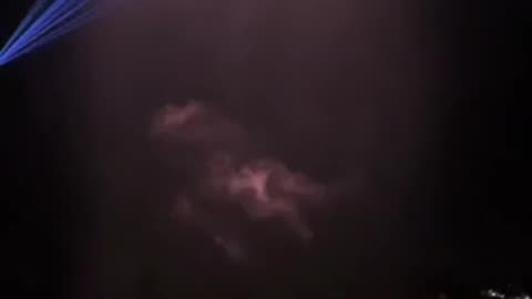 A dramatic waterfall transformed into a glowing curtain of light as lasers paint moving patterns across the falling water