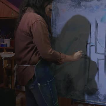 A young woman painting a mesmerizing abstract art piece with a thick brush in her studio