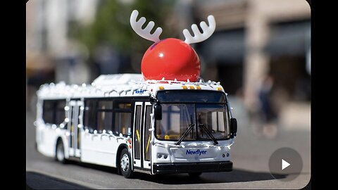 A Newflyer Toy City bus decorated with Christmas lights and a reindeer figure, in an urban setting.