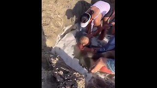 Man stuck in sand pool, as tide come in. People try to free him from drowning.