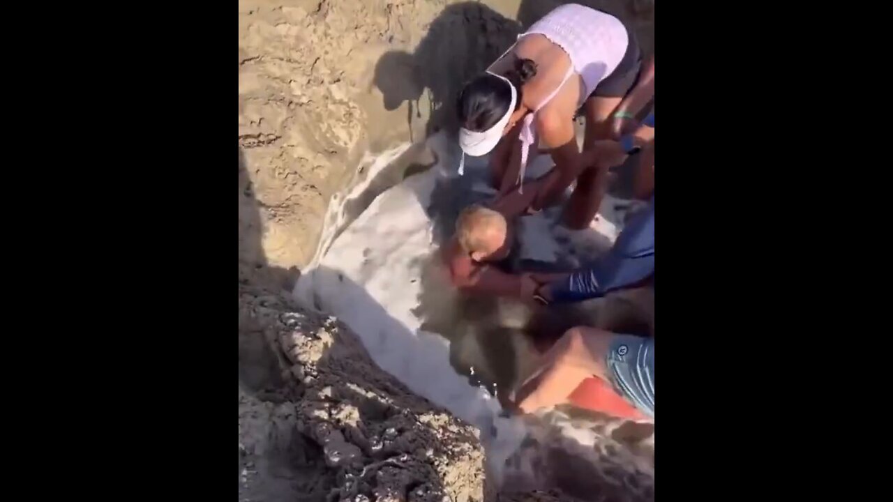 Man stuck in sand pool, as tide come in. People try to free him from drowning.