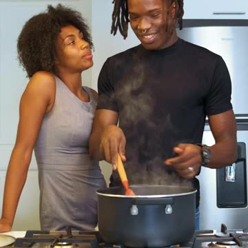 Man cooking is surprised by his wife with a hug