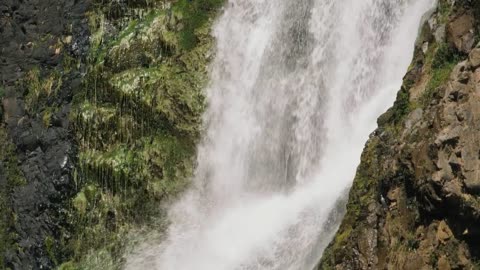 The length of a waterfall, mossy rocks on both sides of the water.