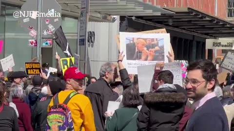 Protester at the "Tesla Takedown" protest in NYC holds a sign showing Trump kissing Elon Musk's feet