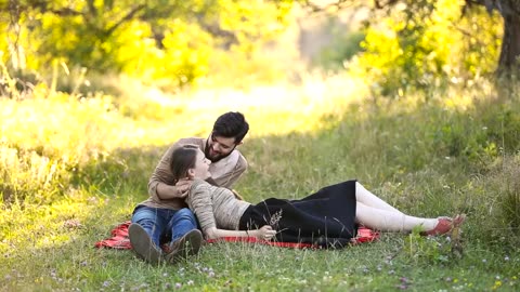 Romantic Young Couple sitting on the grass and kissing