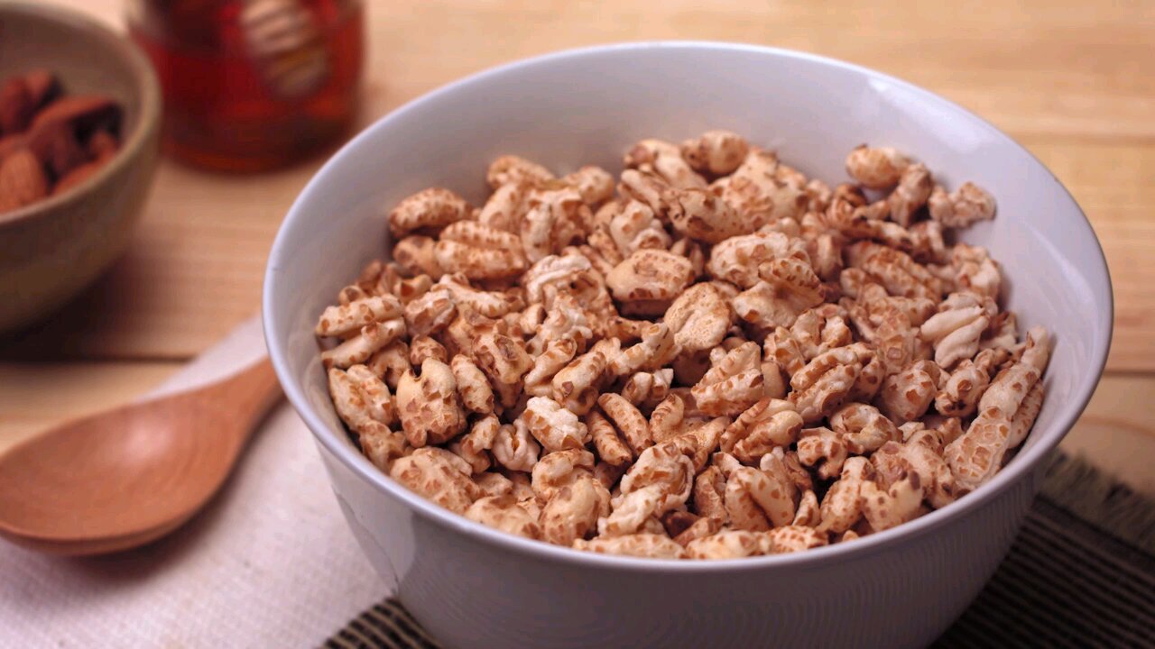A continuous stream of milk cascades in slow motion into a white bowl full of puffed rice cereal