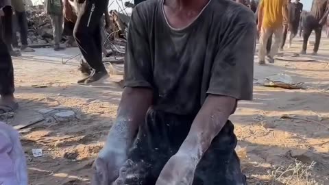 A Palestinian collects the remnants of flour from the ground to feed his hungry children