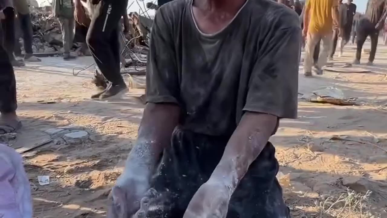 A Palestinian collects the remnants of flour from the ground to feed his hungry children
