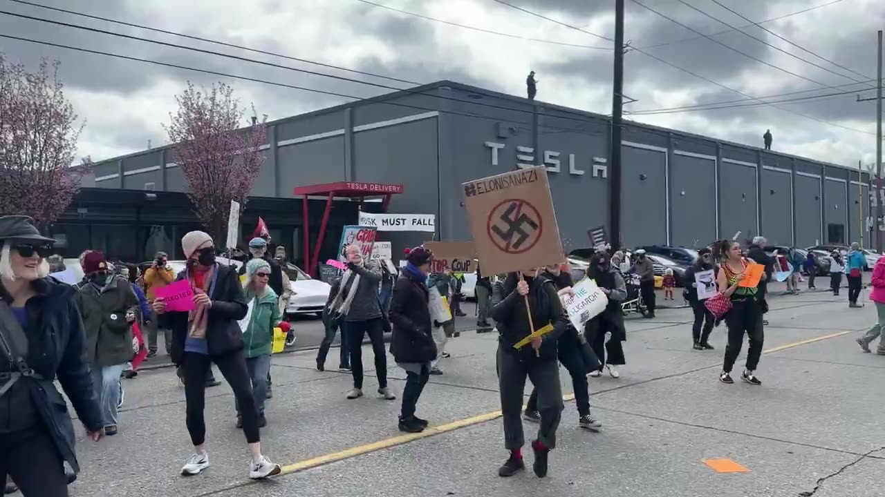 Tesla building security watching overhead as protesters dance on the street