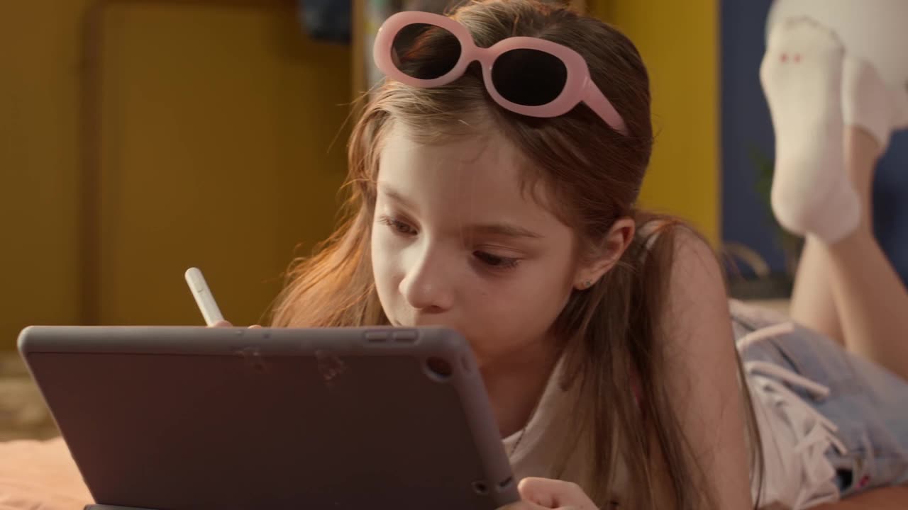 Little girl playing with a tablet laying on her bed