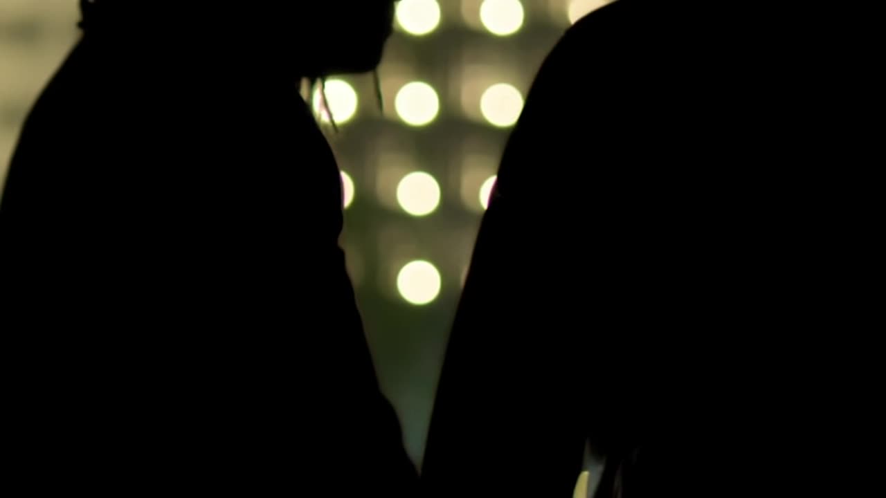 A vertical shot of two men silhouetted against city lights.