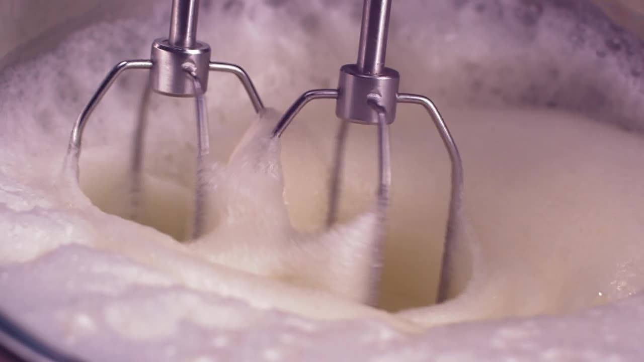 Close-up of whisk blades whipping egg whites until stiff peaks form. Smooth, satisfying motion.