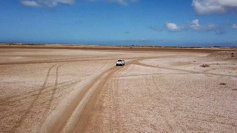 A Pickup Truck Is Travelling On A Desert Road At Daytime
