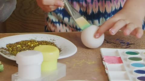 Mother and daughter dampen the brush on the color palette to paint easter eggs