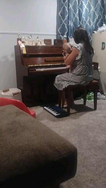 Rebekah playing piano while holding a baby