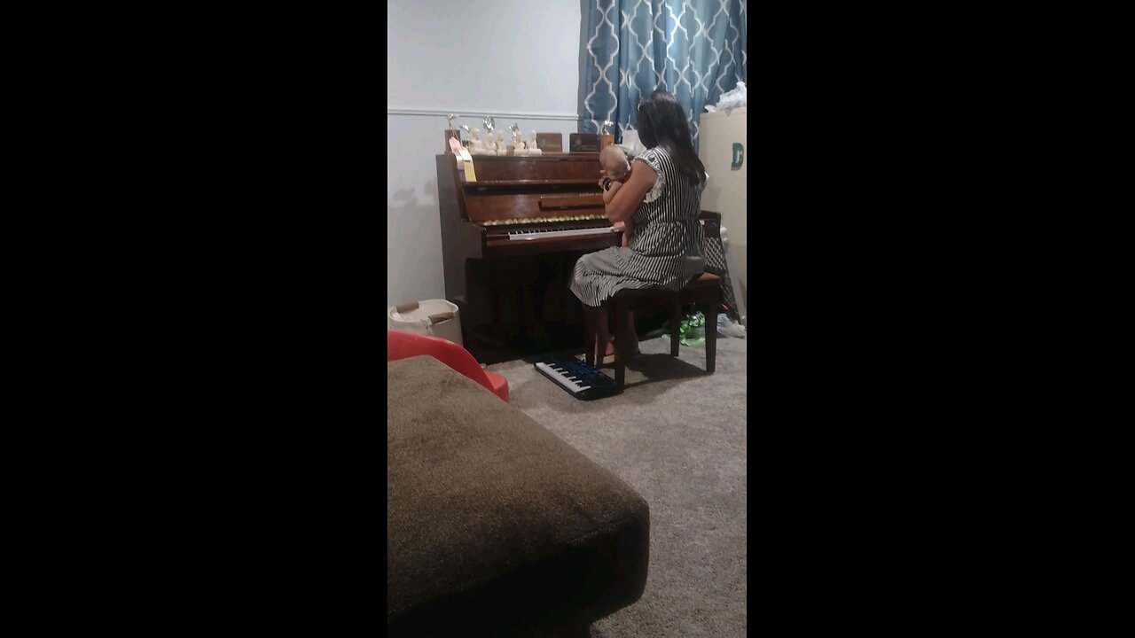 Rebekah playing piano while holding a baby