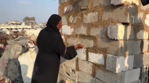 A Palestinian woman in Gaza builds a small handmade shelter from mud and stones