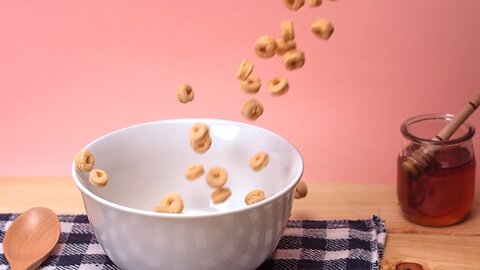 Rings of wheat cereal falling down in slow motion into a white bowl placed 🥣