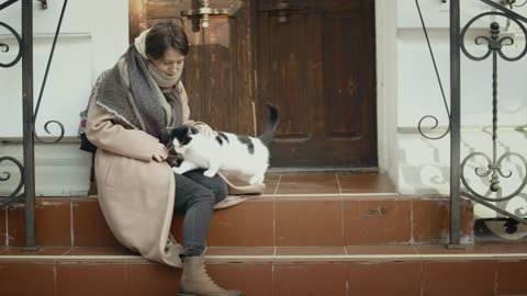 Young woman playing with a kitten on the steps of a house