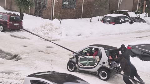 People Help Push A Mini Car Out Of The Snow