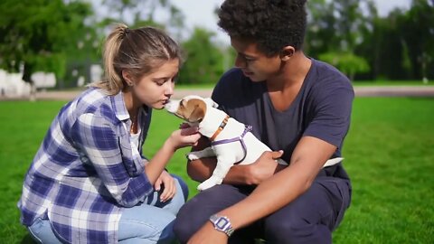 Two multiracial young friends sitting on the green grass in park enjoying the day while holding cute