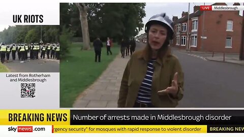 Armed Migrants Walk Behind A Reporter As She Discusses "Far-Right" Protestors