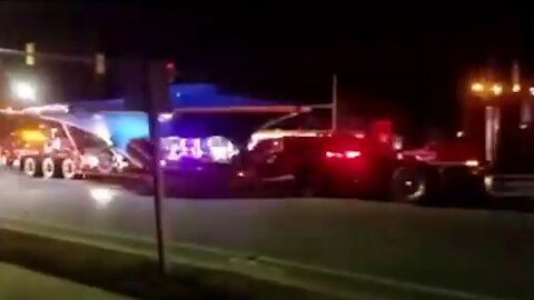 This is view of a truck carrying a UFO passing by with a police car theme park or otherwise [Space]