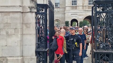 Armed police officer pulls tourist back by his back pack getting in the way of the kings guard