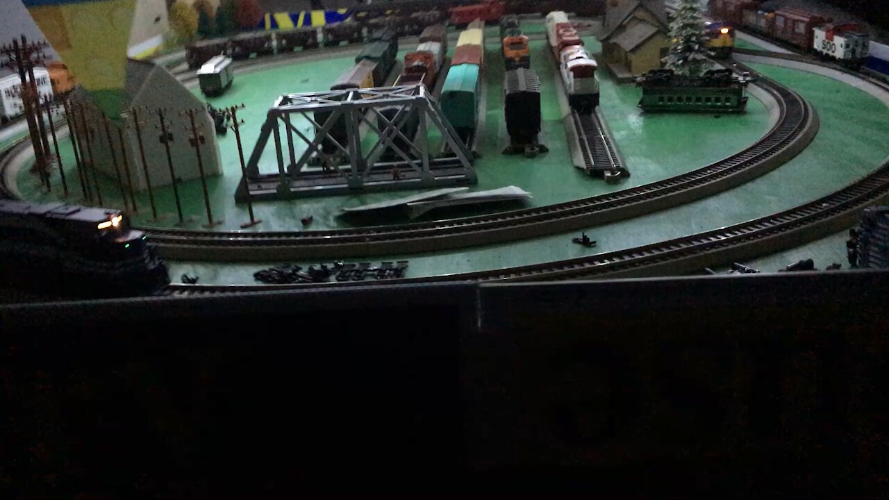 Three trains running around the layout at night with lights on the HO deck