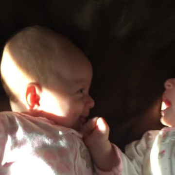 Newborn twin girl amused by crying sister