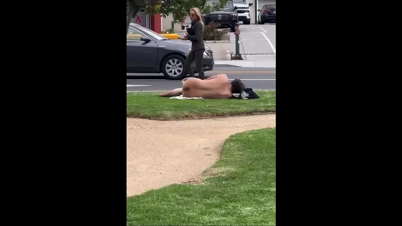 Nude homeless man lounges out on the grass in LA as women walk by