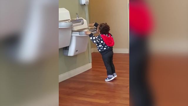 A Tot Girl Struggles To Drink From A Water Fountain