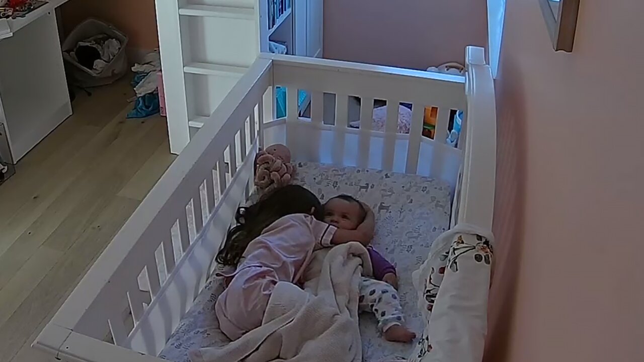 Sweet Little Girl Cuddles Baby Sister In Her Crib