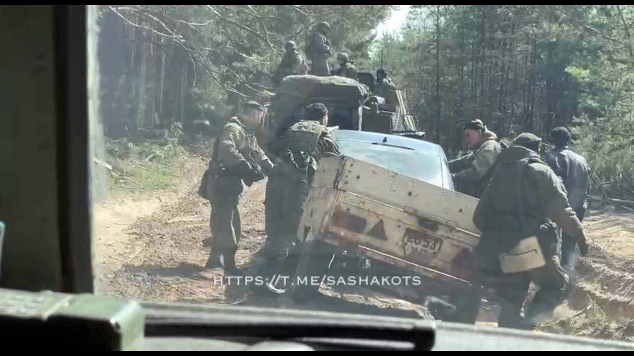 Russian military help a local free their car stuck in mud on a forest road