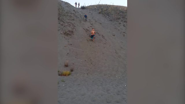 A Little Boy Flips Over While Running Down A Sand Dune