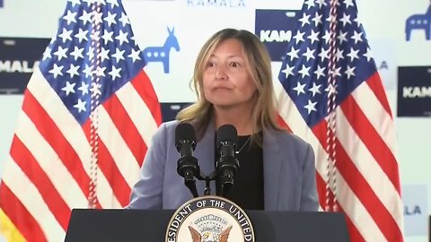 Pay attention to the body language of the woman at the podium; she knows something is wrong