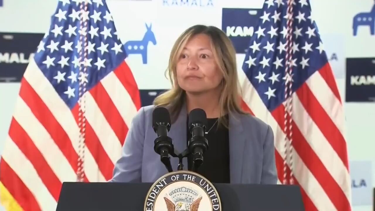 Pay attention to the body language of the woman at the podium; she knows something is wrong