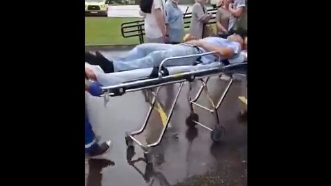 People STILL wait in line to get a shot, while an injected person is carried away by ambulance