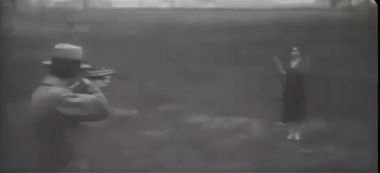 A man testing bulletproof glass by shooting it while his wife holds it.