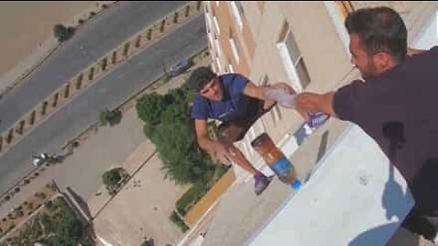 Young man does "bottle flip challenge" hanging from building