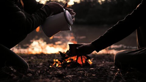 People pouring a warm drink around a campfire.