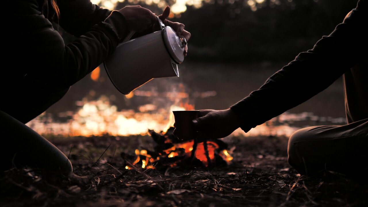 People pouring a warm drink around a campfire.