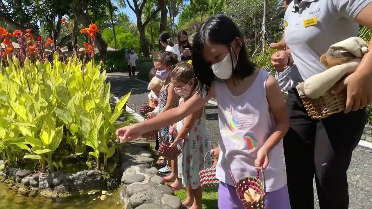 Nanny teaches children how to feed fish in the pond. All in a face mask. Kind activities for childr