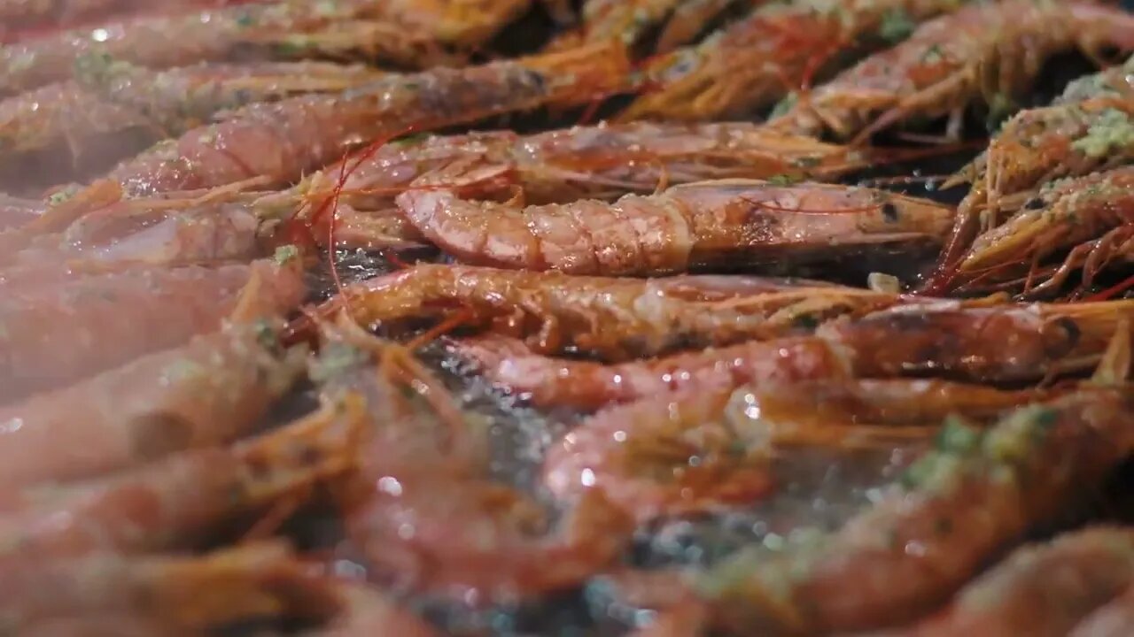 Closeup chef hands flipping crawfish with metal tongs on grill. Man hands cooking seafood with herbs