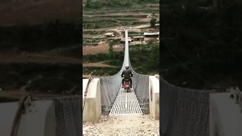 Sign Painter Sean Starr riding a motorcycle across a suspension bridge in Nepal.